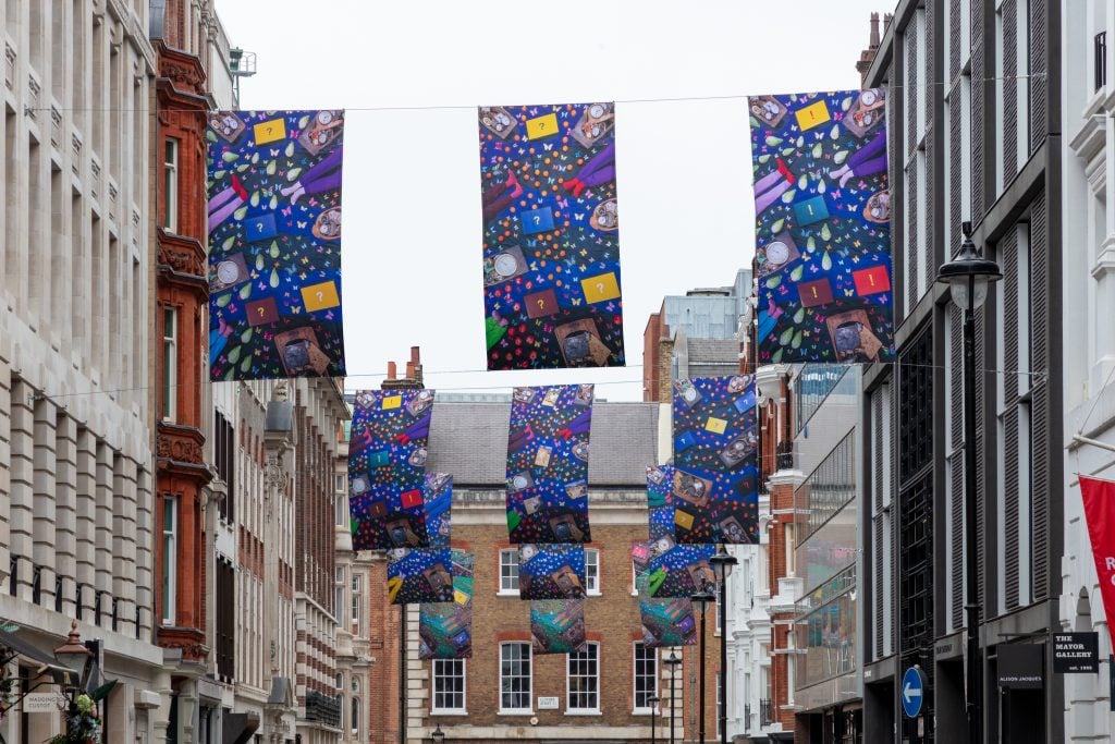 Banners in blue and other colours suspended in the air on Cork Street in London.