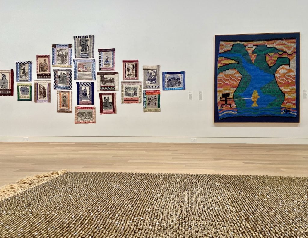 image of a woven rug made with 30,000 bullet casings under wall-hung tapestries and textile works