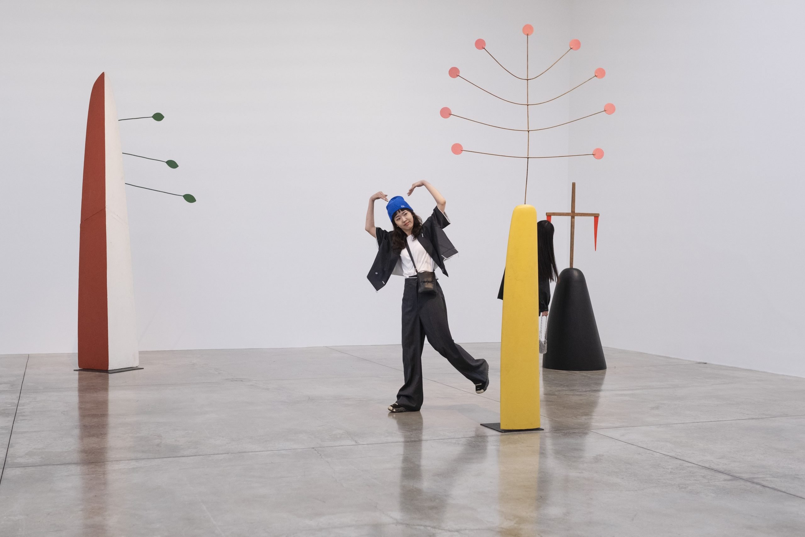 An art exhibition goer posing a heart-shaped gesture in a gallery.