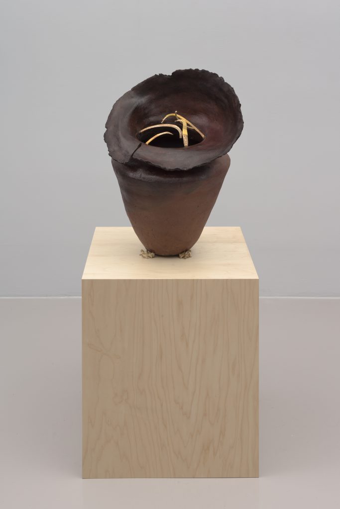 photograph of a vase sculpture on a wooden pedestal