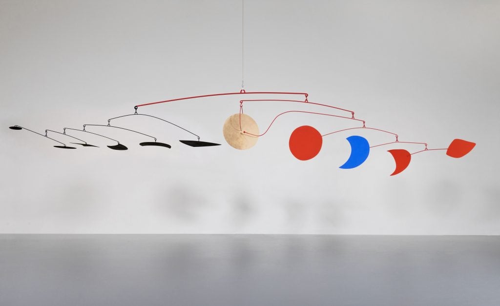 A large mobile hung with various geometric cut-outs in red, blue, gold, and black