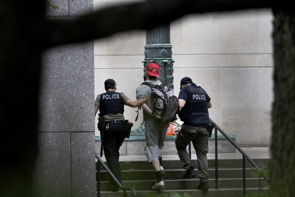 A man in a backward baseball cap being led away by two police officers