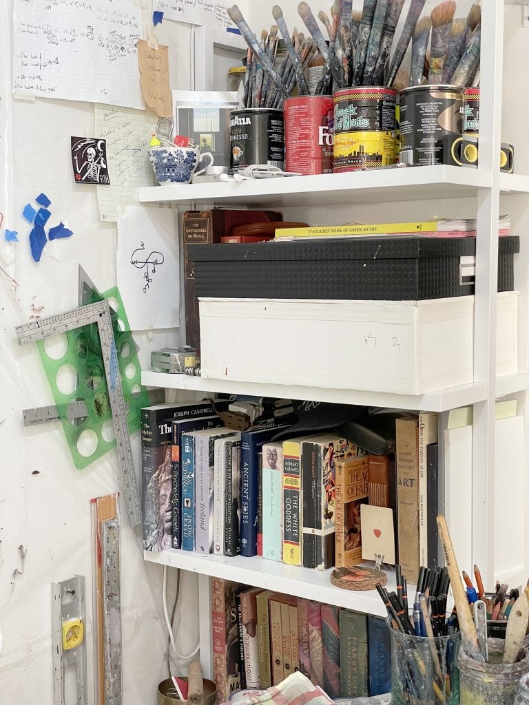 a photo of a bookshelf with books, paint brushes, and boxes