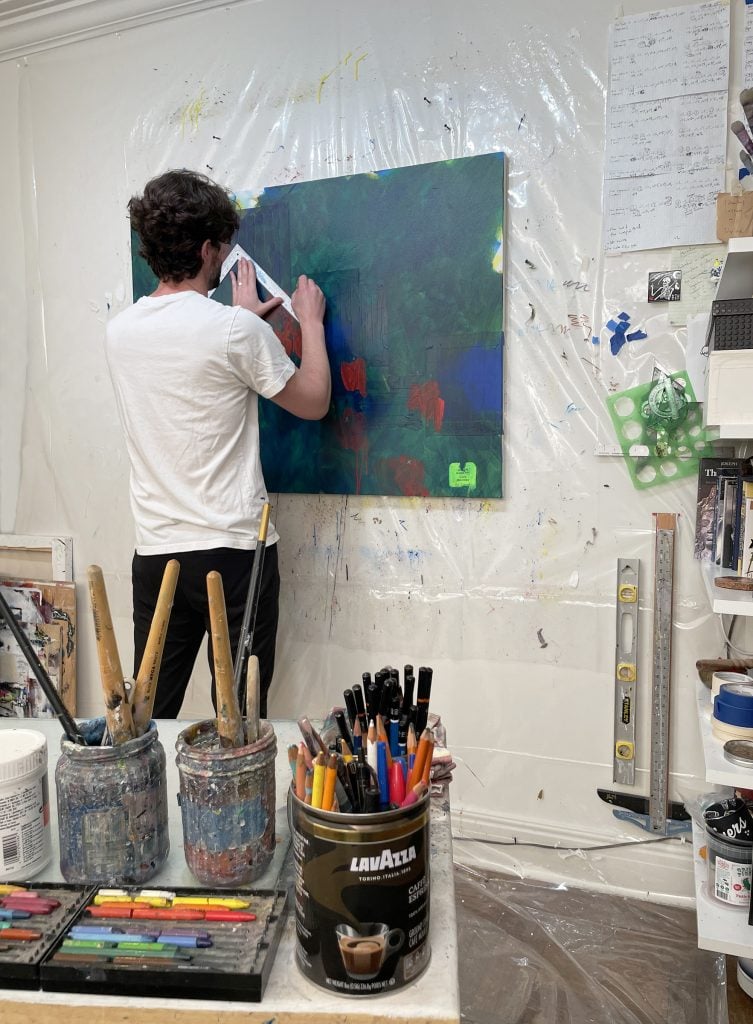 a man in an artist's studio stands before a painting and draws on it