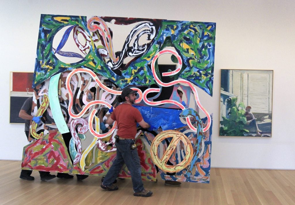 Art handlers carry a large aluminum sculpture with swirling cutoutsby the artist Frank Stella
