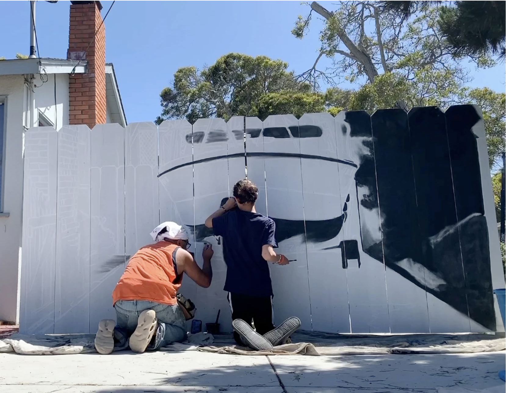 Two men at work painting a boat on a fence