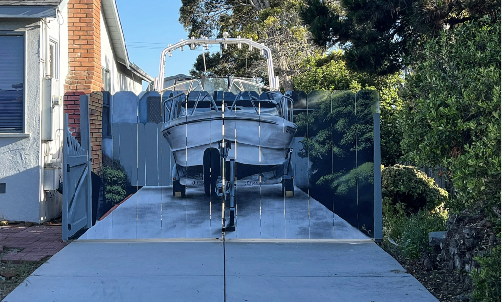 A fence hiding a boat in a driveway has a boat painted on it by artist Hanif Panni