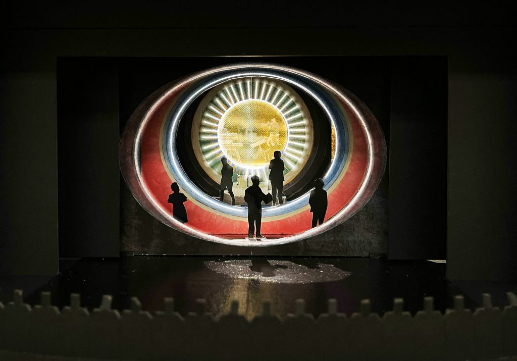 A mock-up of a theater set showing concentric circles, with cut-out figures standing amidst the arcs.