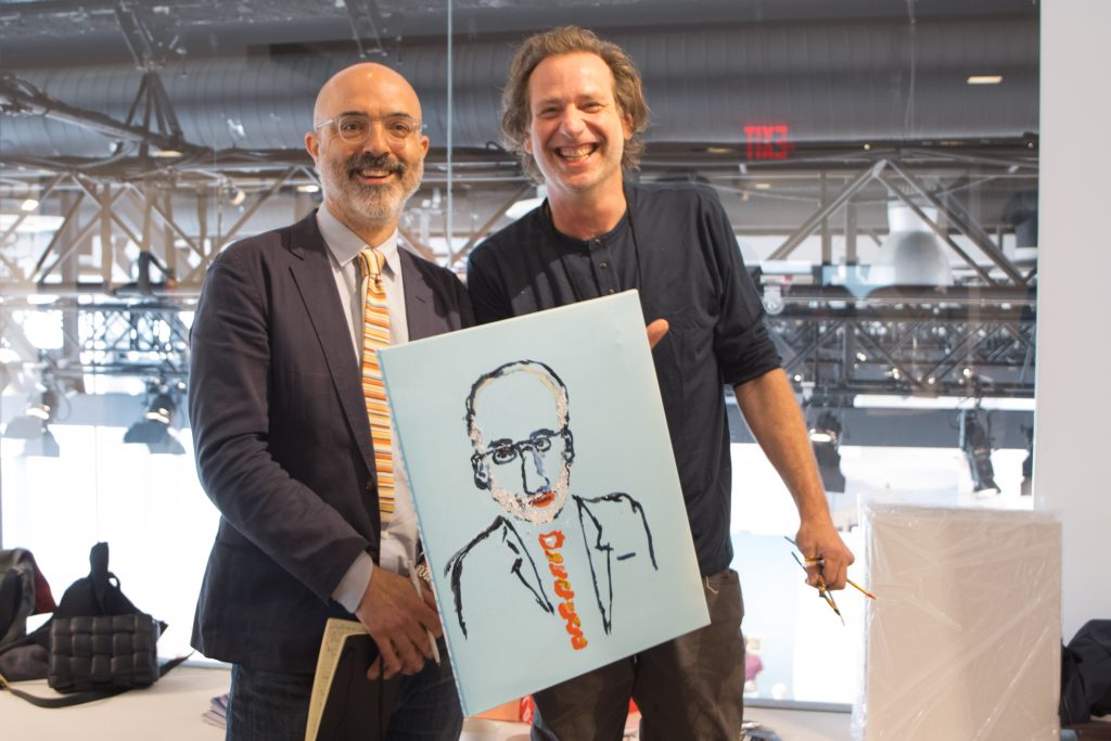 Two men standing and smiling, while holding on to a portrait