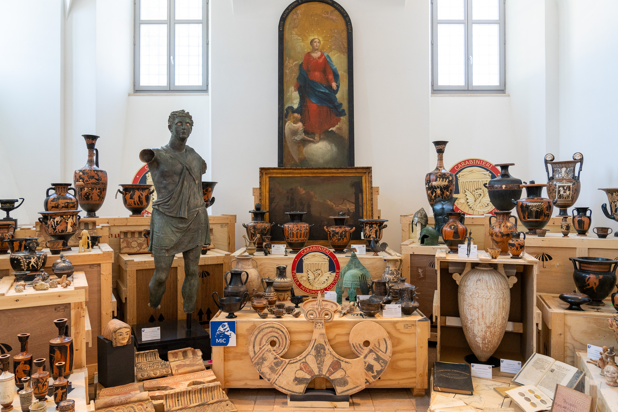 A gallery full of ancient artifacts including a large statue, an altarpiece, and boxes laden with small ceramics and sculptures