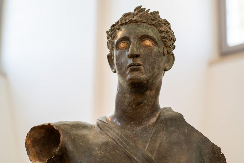 Close-up of the face of a bronze statue of a man with an arm missing