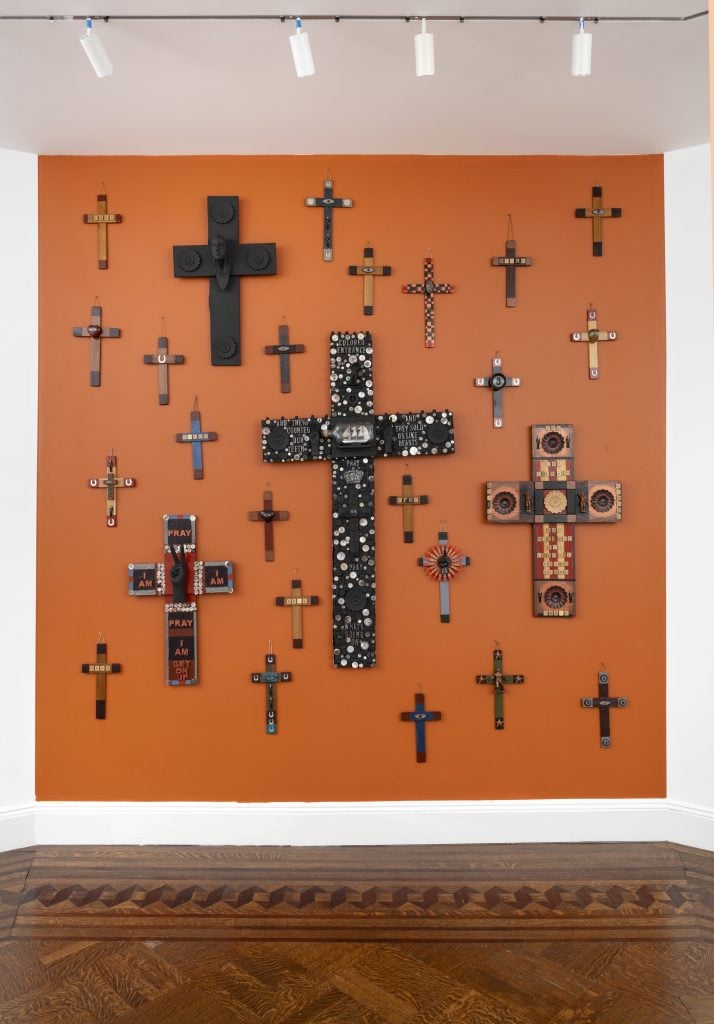 photograph of varying sizes of cross sculptures hanging on a orange wall