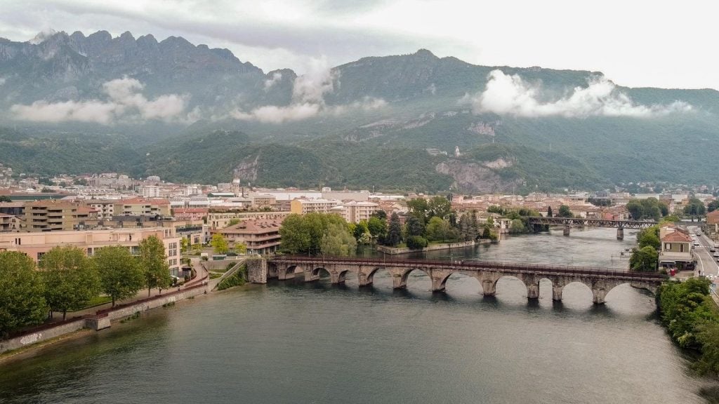A photograph of a mountainous Italian landscape with a body of water and a bridge, where the Mona Lisa was purportedly painted