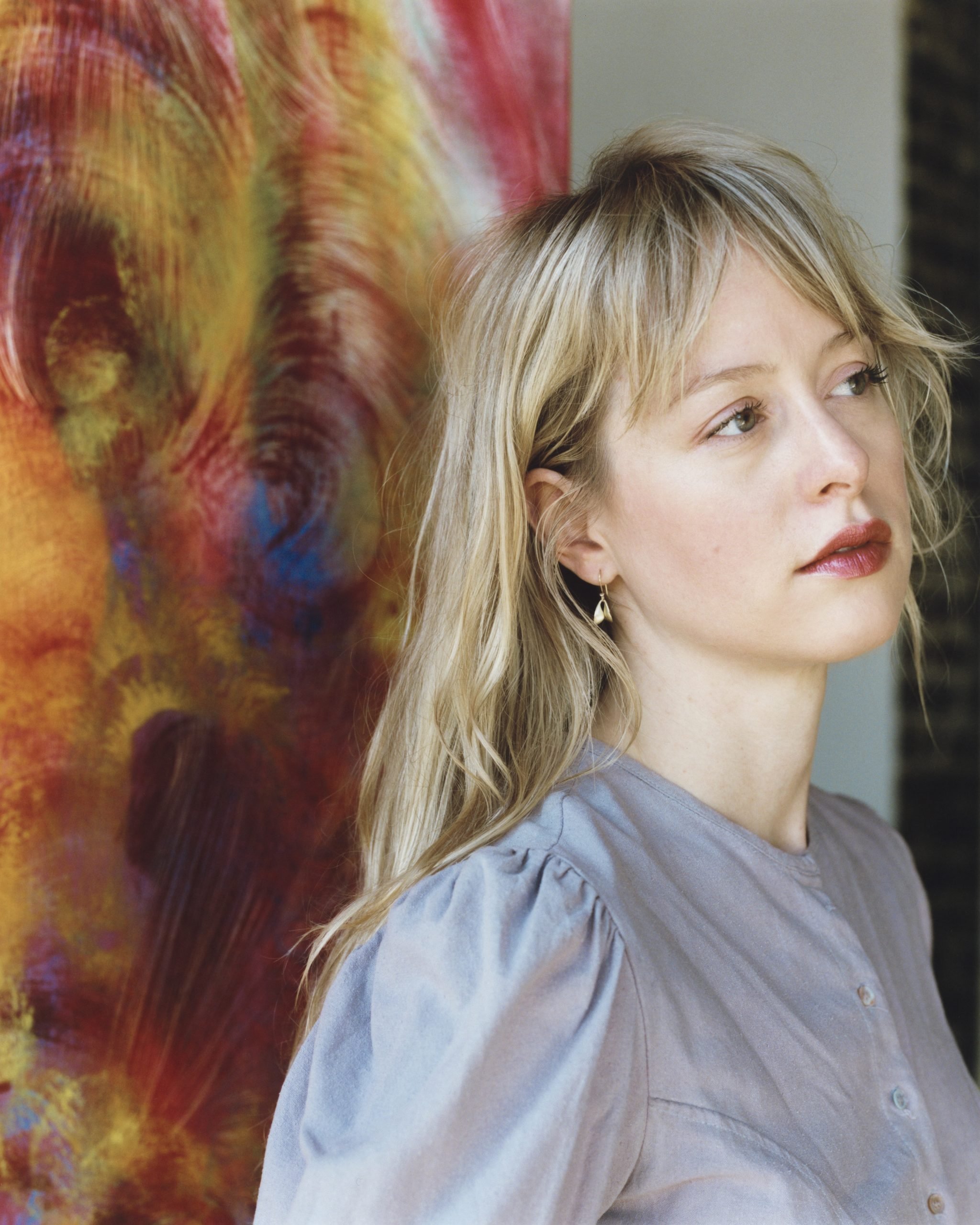 a woman with blonde hair looks off to the right. she is wearing red lipstick and a pale lilac blouse.