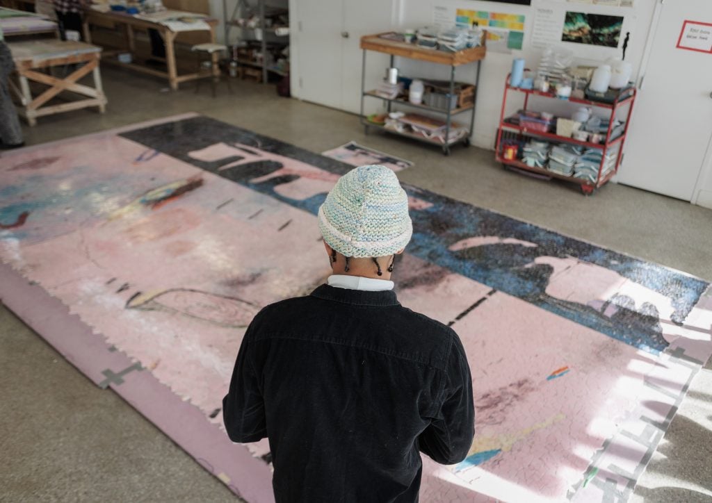 photograph from behind of artist manuel mathieu looking at his work layed out on the floor