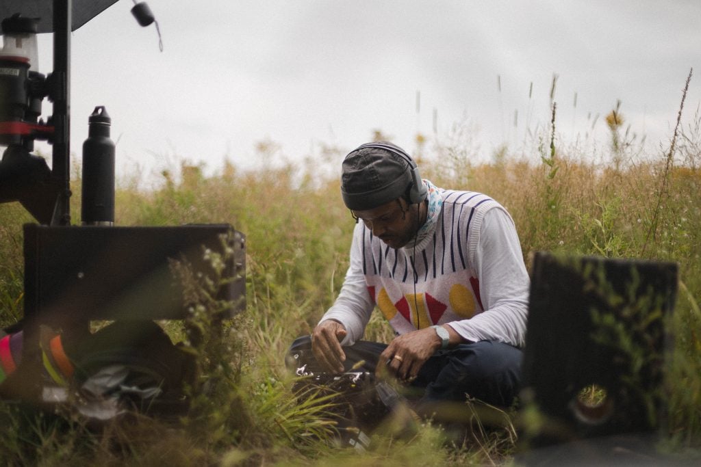 photograph of artist manuel mathieu in a field of grass sitting down with headphones