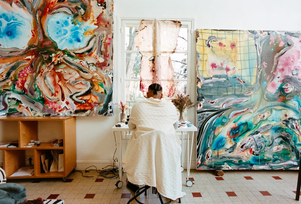 photograph of artist Manuel sitting by a window with artwork in the studio in Paris