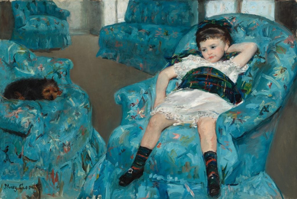 A little girl in a dress sits in a blue armchair