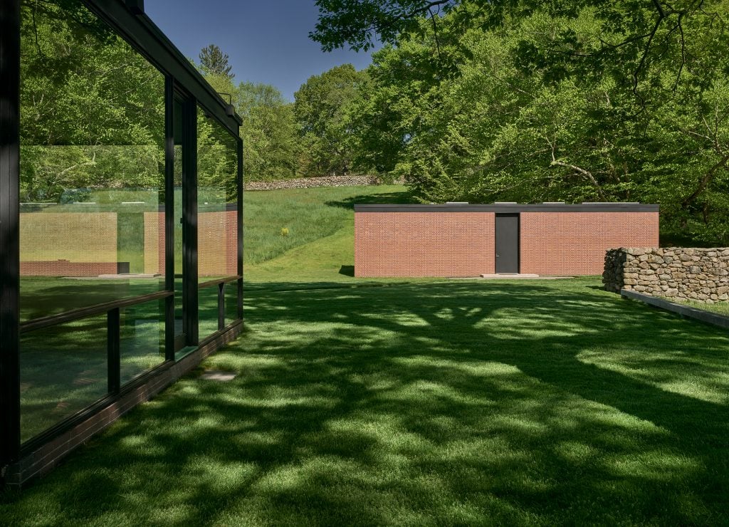 A squat, rectangular brick building designed by Philip Johnson beside a glass-surfaced house