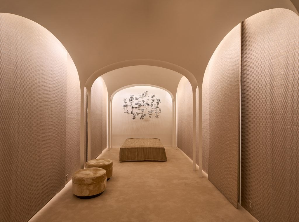 A bedroom designed by Philip Johnson with plaster arches, a bed and stools, and a wire sculpture on the wall