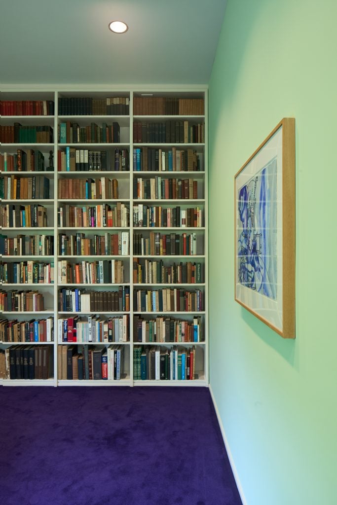 A mint green room designed by Philip Johnson with a bookshelf built into one wall and an artwork hanging on another