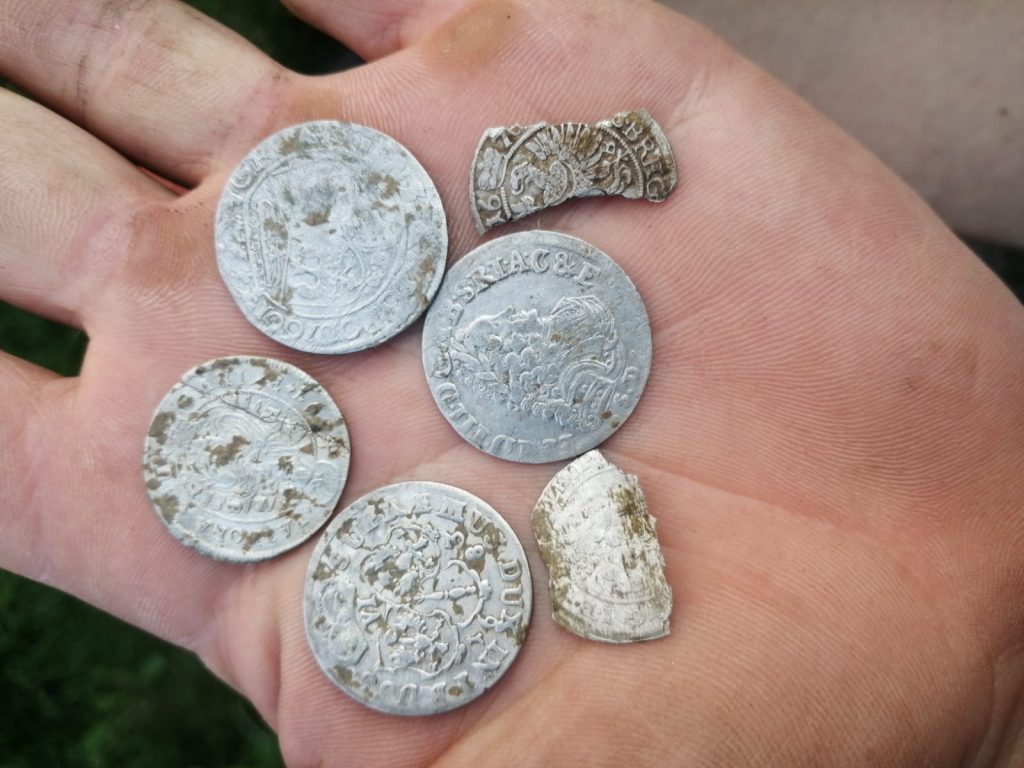 A person's palm holding six ancient silver coins