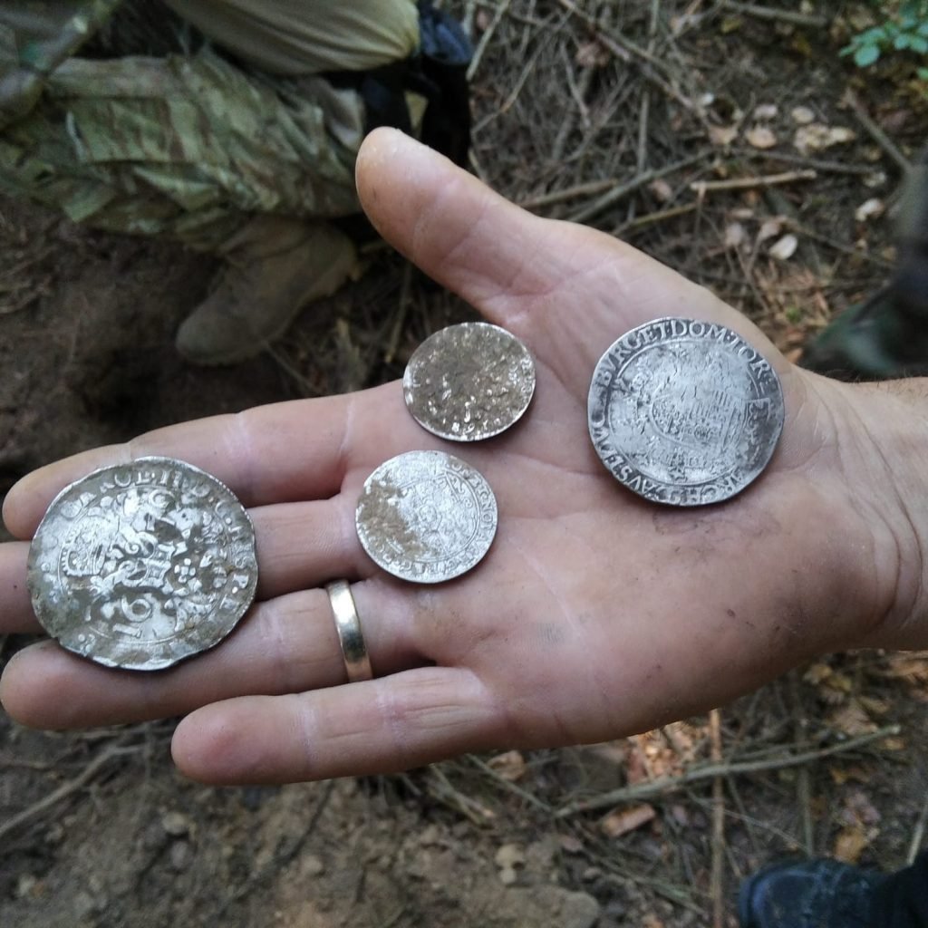 A person's palm holding four ancient silver coins
