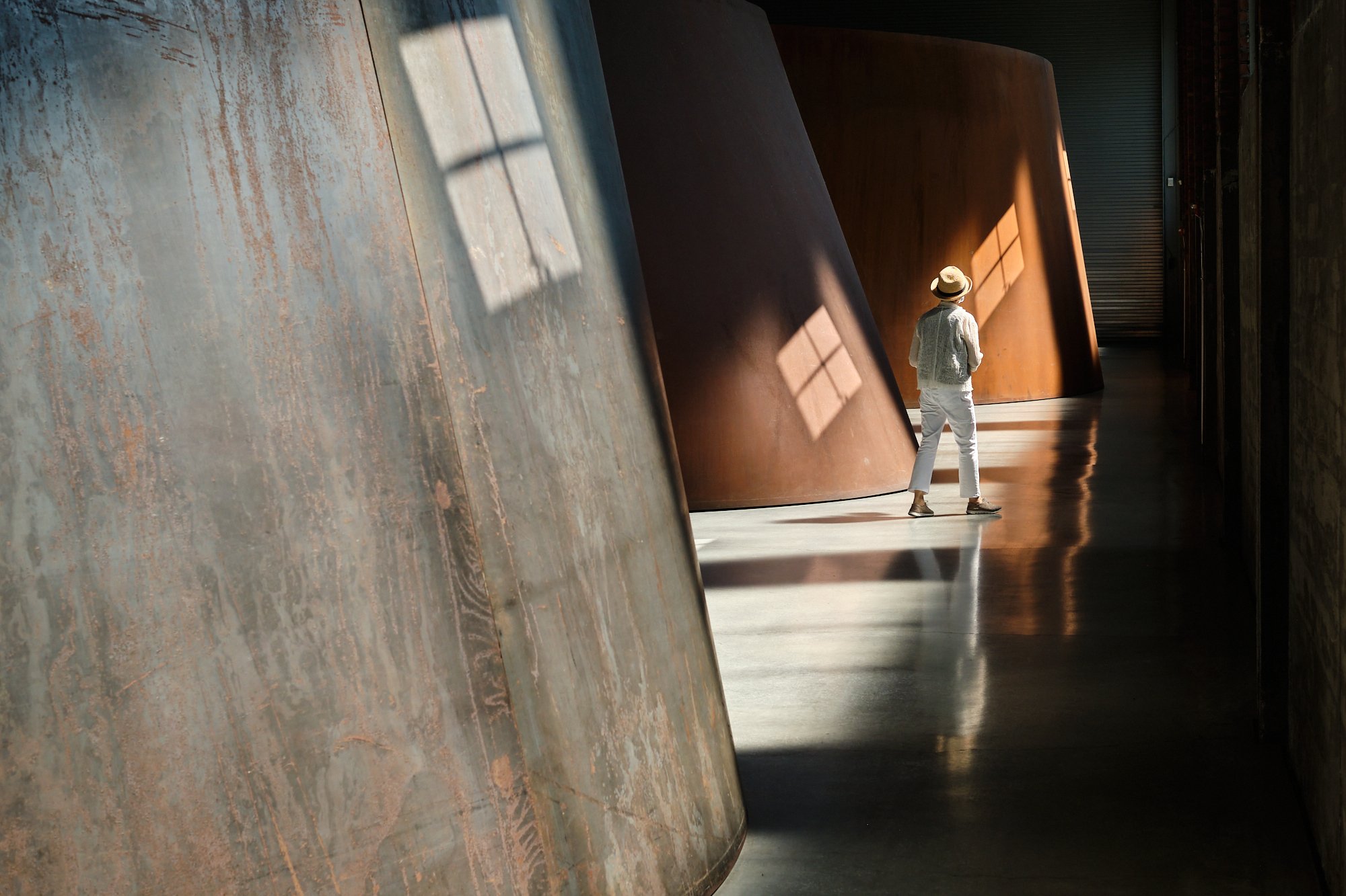 Visitor walking among monumental steel sculptures installed at Dia Beacon, with the shadows of windows cast on them. Dia Art Foundation.