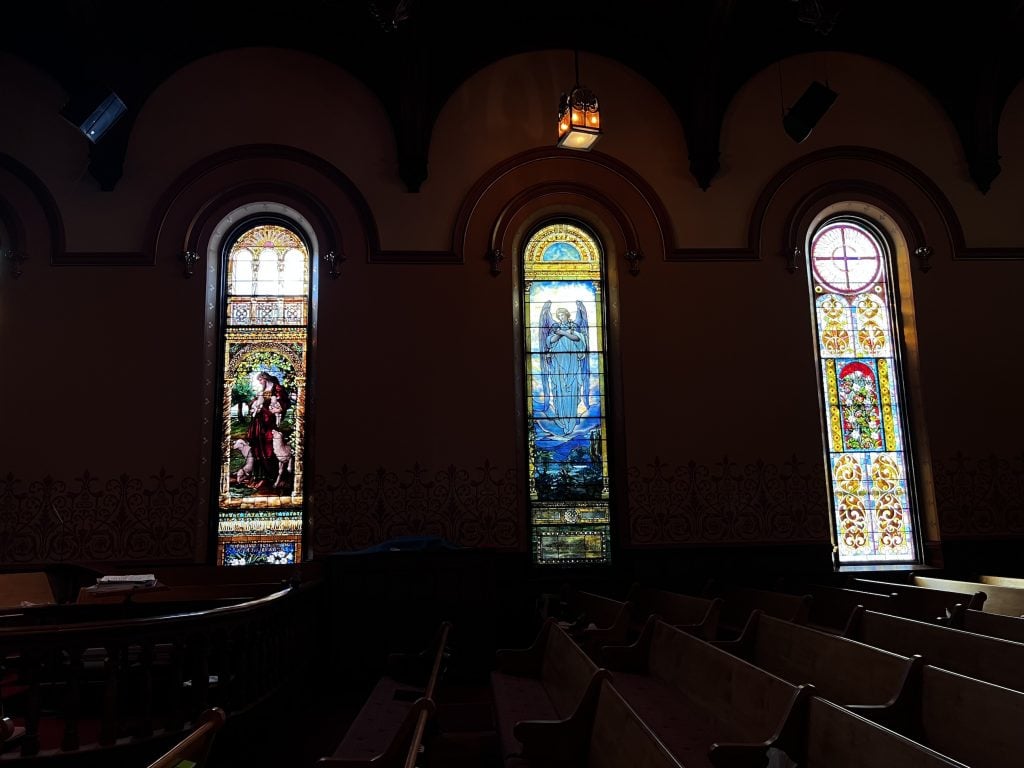 Three stained glass windows in a darkened church