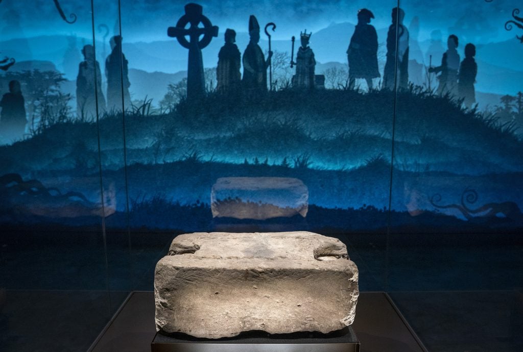 A rectangular chunk of rock on display in a gallery with a blue-lit backdrop