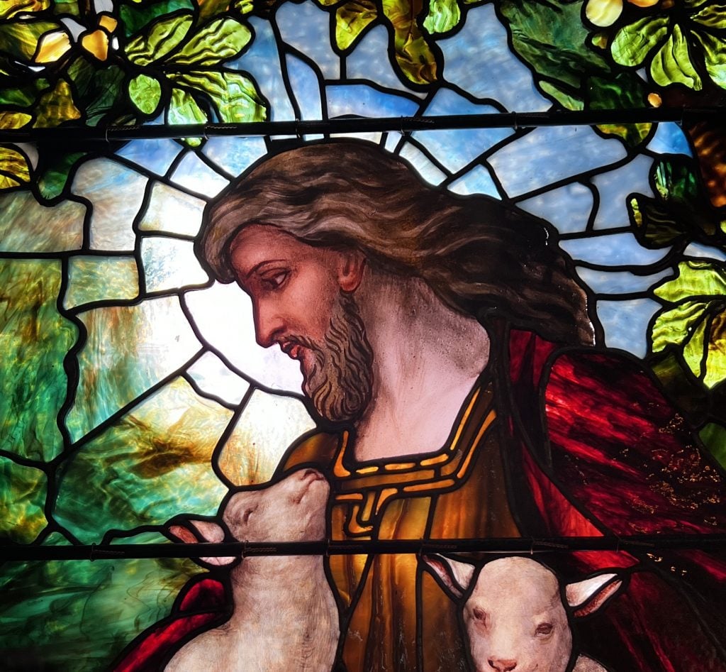 A stained-glass window showing Christ as a shepherd holding two lambs