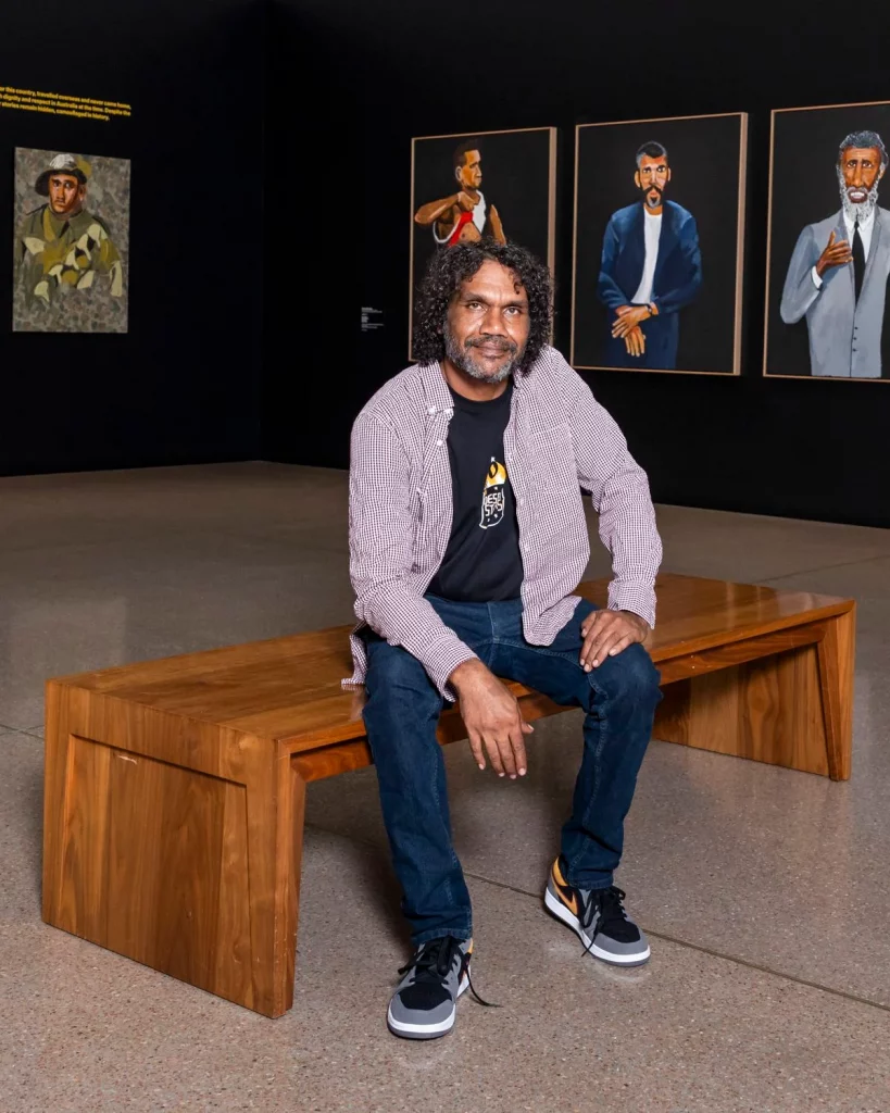 A man sitting on a bench in a gallery hanging with portraits
