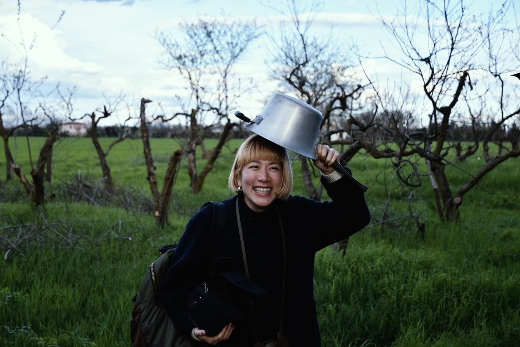 portrait of artist yuko mohri smiling at the camera holding a pot over her head