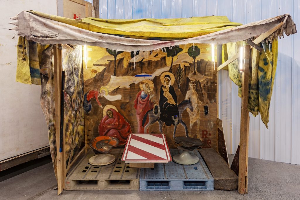 a lean-to made of shipping palettes and dyed cloth with images on it