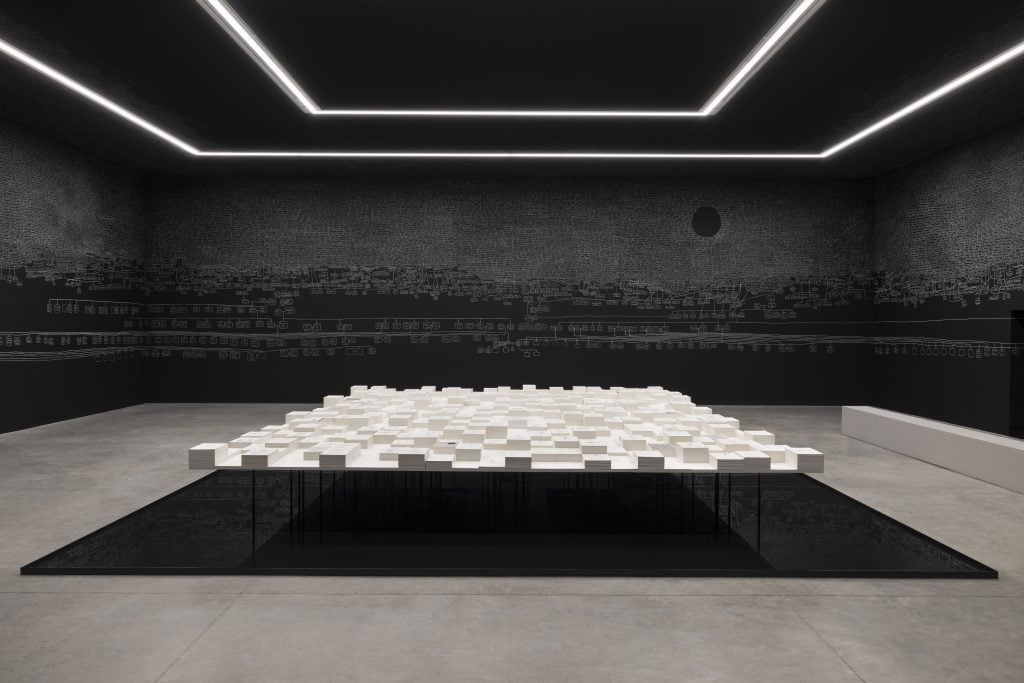 A big space surrounded by black walls with a white installation in the middle