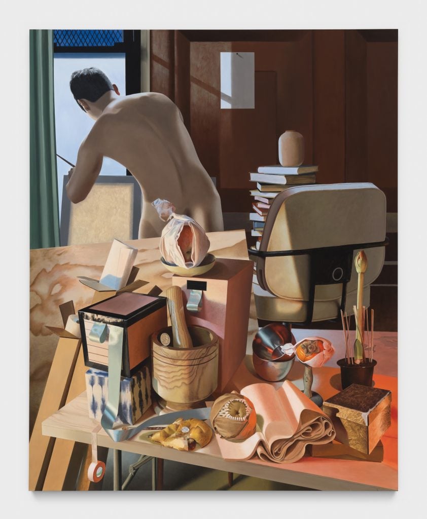 a nude man seen looks out of the window of his studio, we see him from behind, in front of him is a desk and chair filled with books, fruits, a blooming plant, a mortar and pestel etc