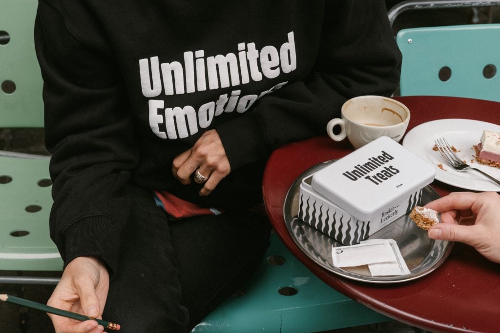 a person in black sweatshirt at a coffee table with cake and treats.
