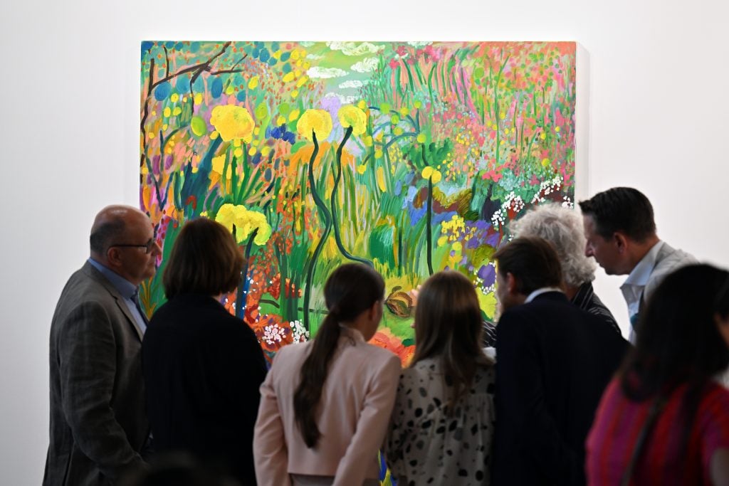 a crowd of people look at a colorful painting of flowers