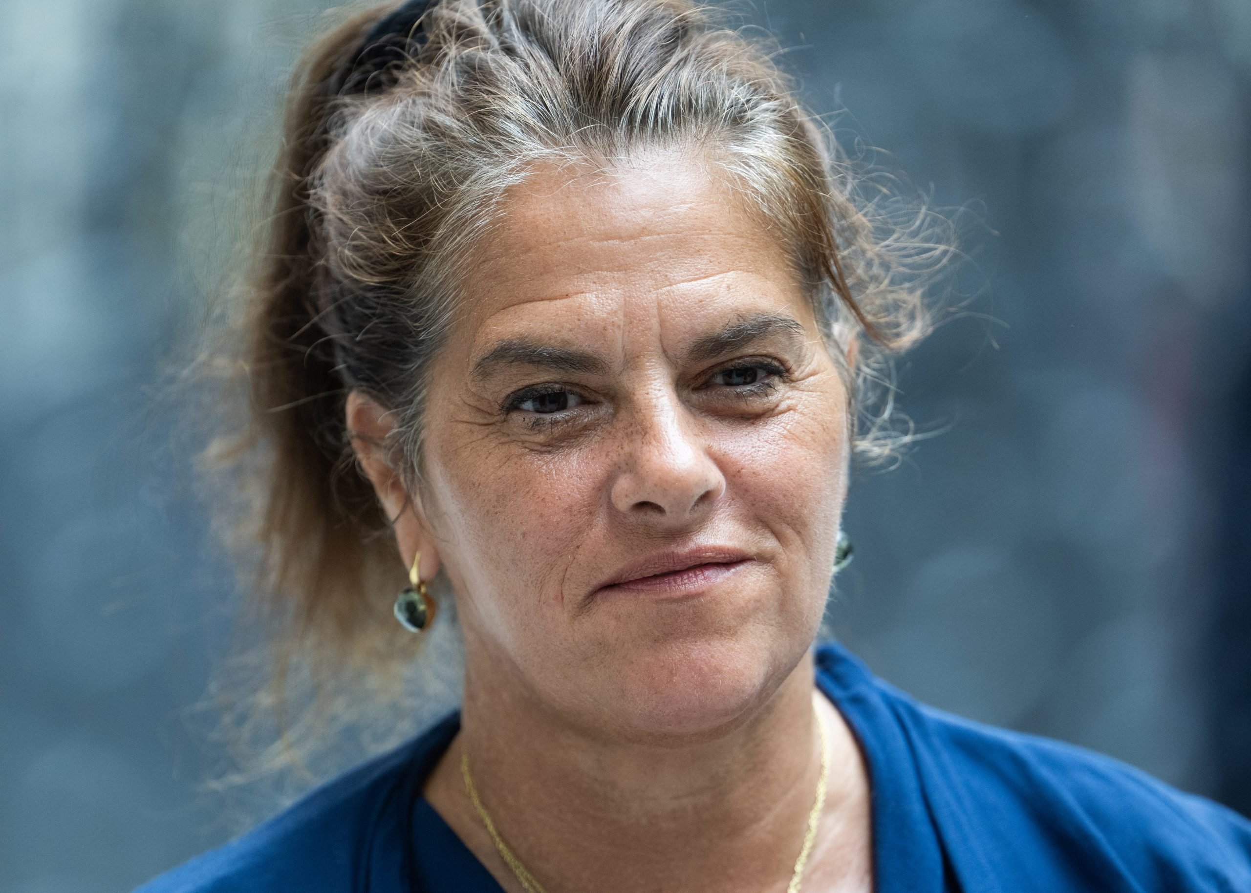 a close up photograph of a woman with her hair tied up wearing a blue top and looking at the viewer