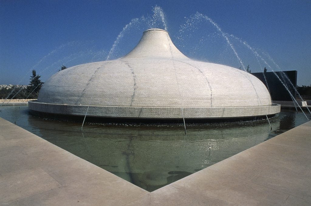 a building shaped like a shallow dome within a fountain against a blue sky