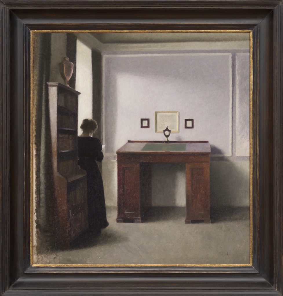 an image of a woman standing in a room with her back to the viewer in front of a writing table