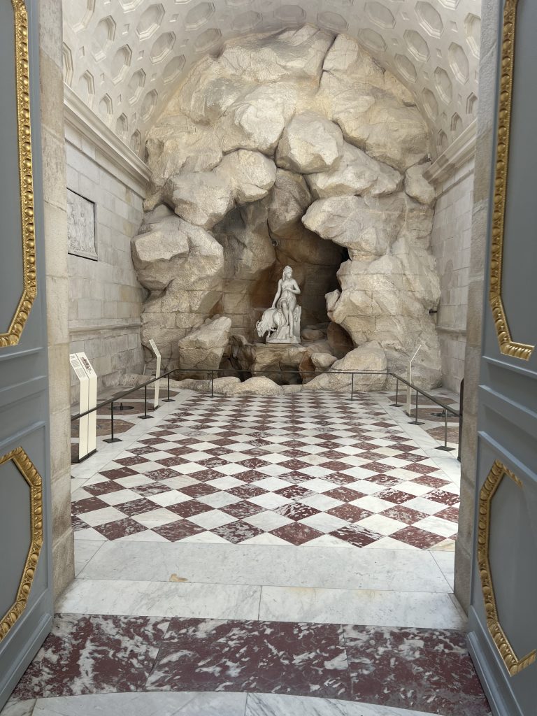 Opulent marble floors and decorated doors lead into a room with a grotto