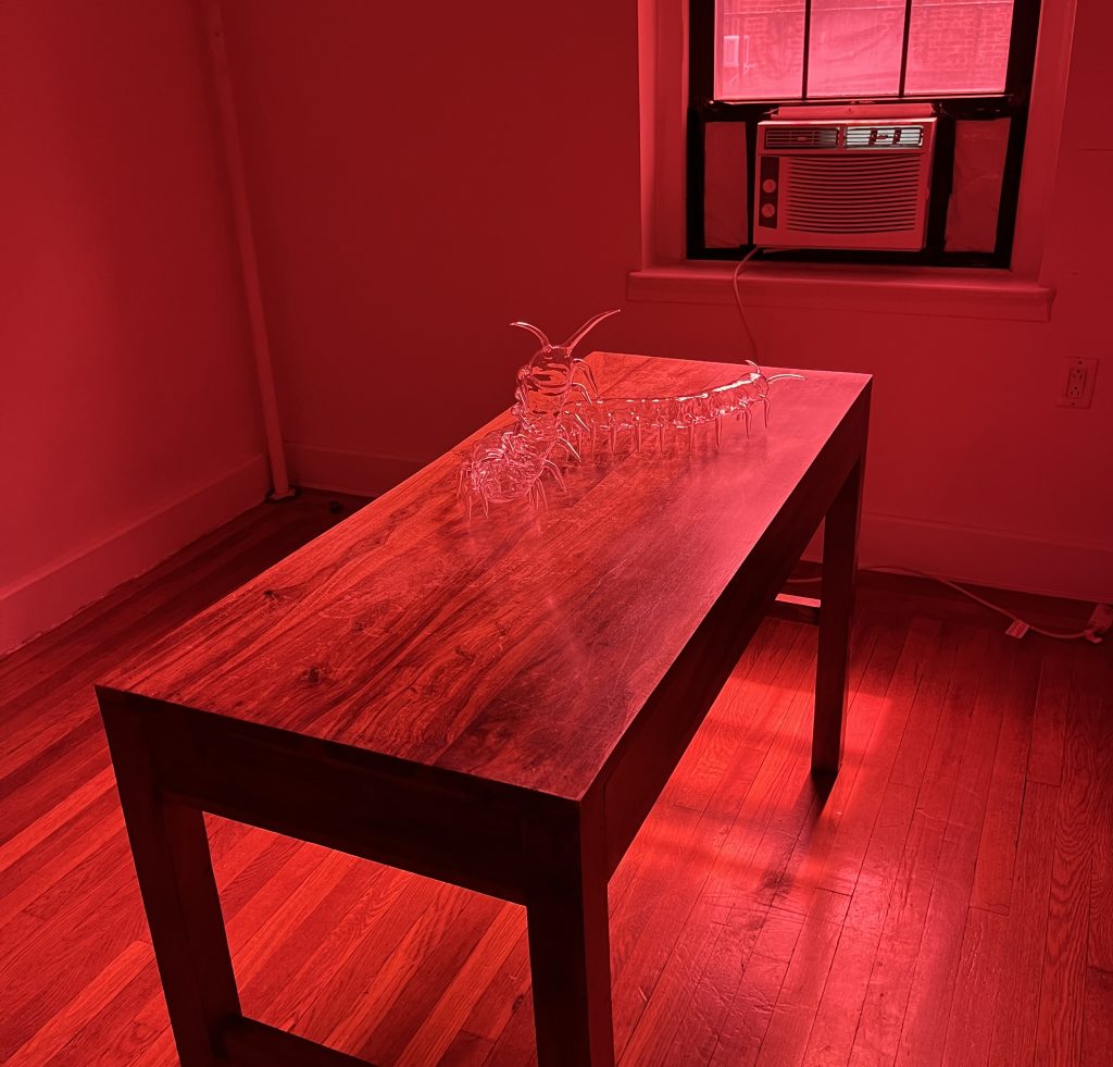 In a color photo, a long wooden table holds a strange glass ssculpture.