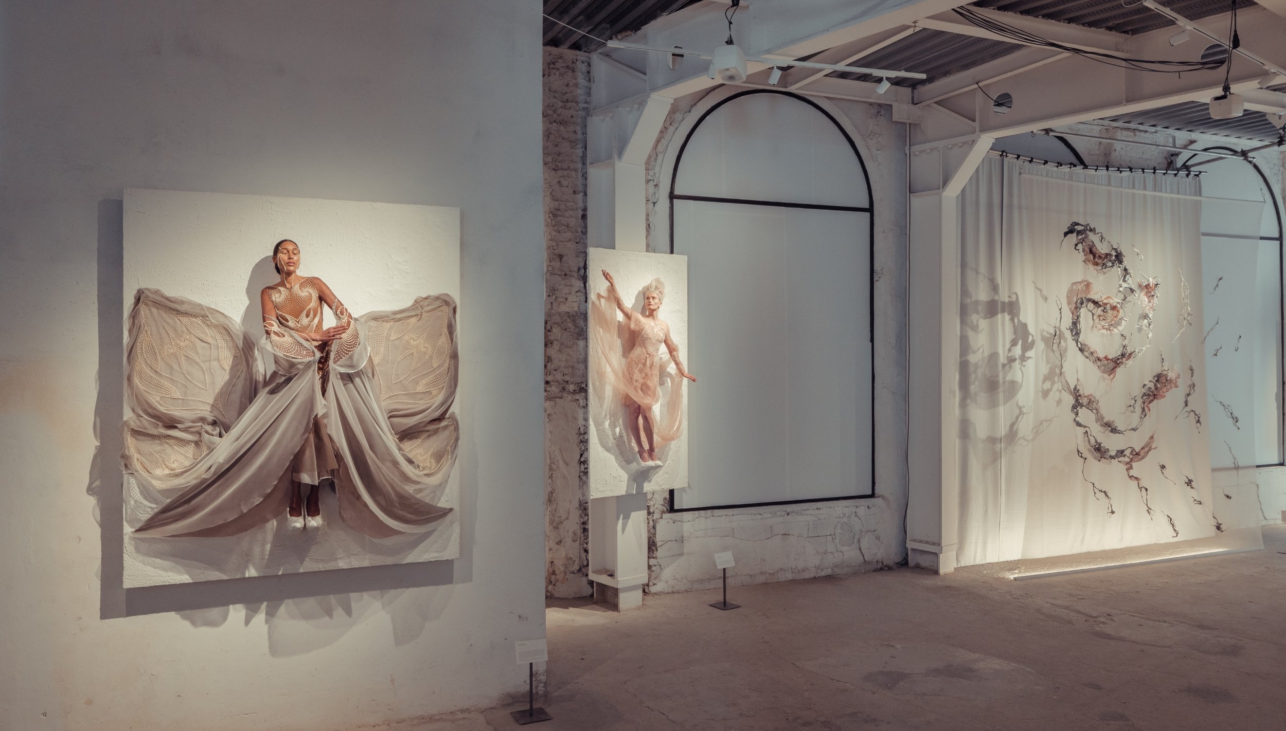 three women are attached to the white planes on the wall, they appear to be floating, they are wearing floating high couture dresses