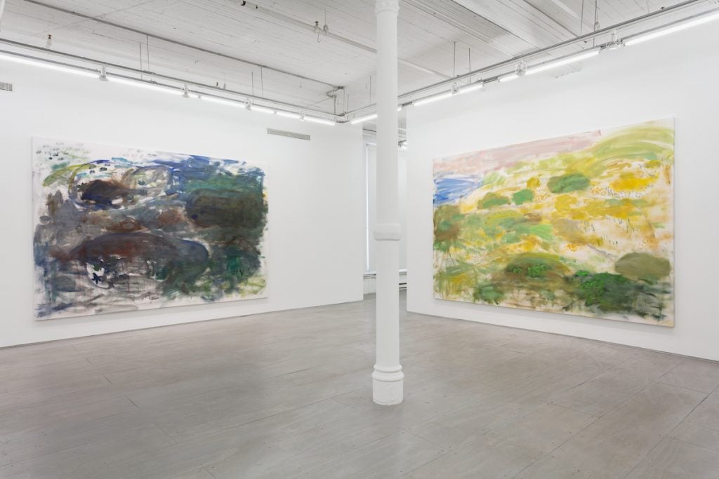 Two white walls in a gallery each hold one large painting of a landscape made with brushy, impressionistic marks