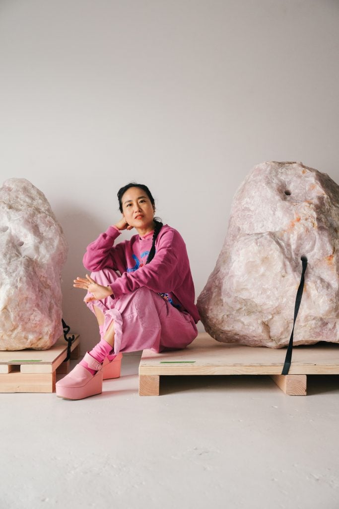 a woman in pink from head to toe sits beside to giant pieces of rose quartz