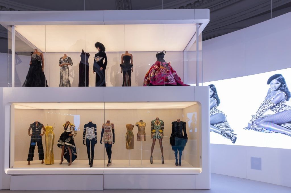 a double tiered glass display cabinet inside which there are lines of mannequins wearing couture gowns