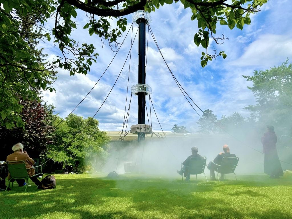 People on a lawn watch a mysterious tower rising from a cloud of mist