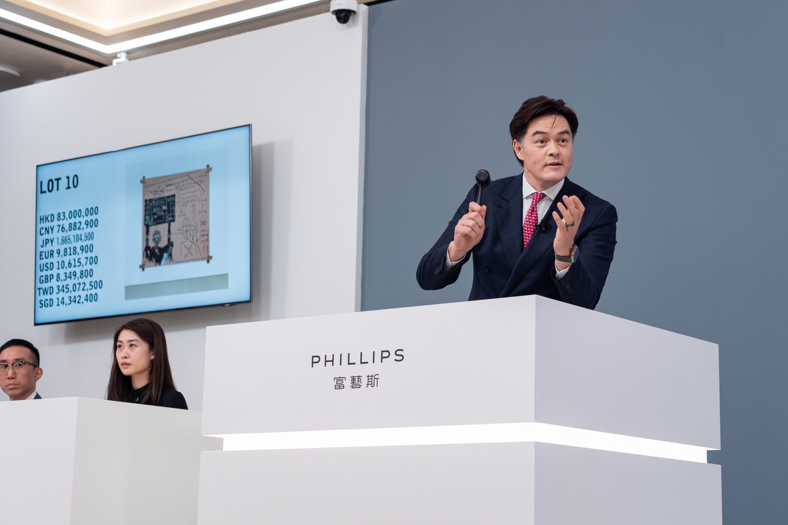 In a color photo, a man in a suit stands and wields a hammer