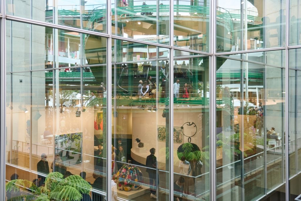 A color photo shows art, art fair booths, and plants amid glass.